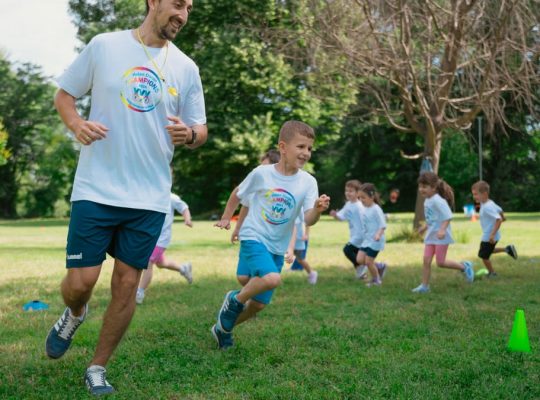 A group of kids running with an instructor during outdoor sports activities on a sunny day in a park.