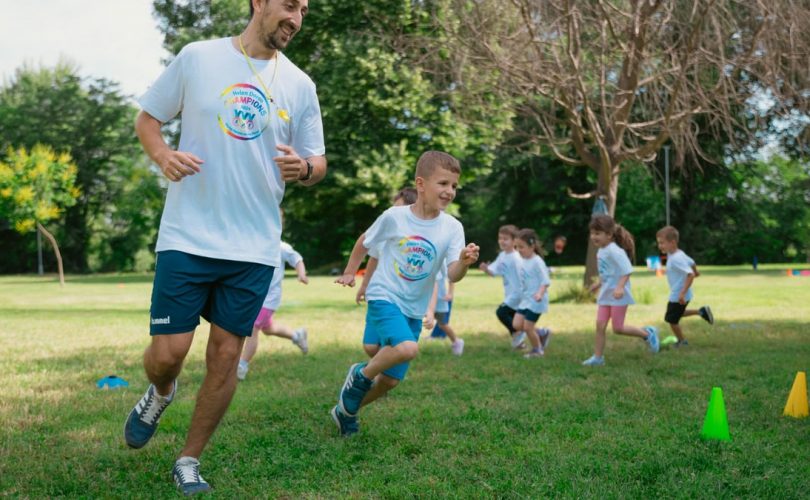 A group of kids running with an instructor during outdoor sports activities on a sunny day in a park.
